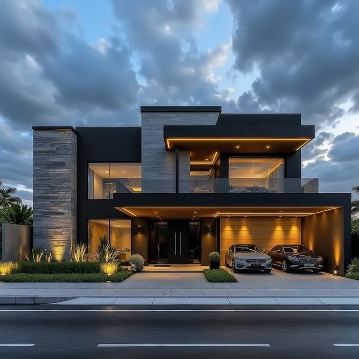 Residence 04 at dusk: a charcoal and slate facade with a warmly lit carport.